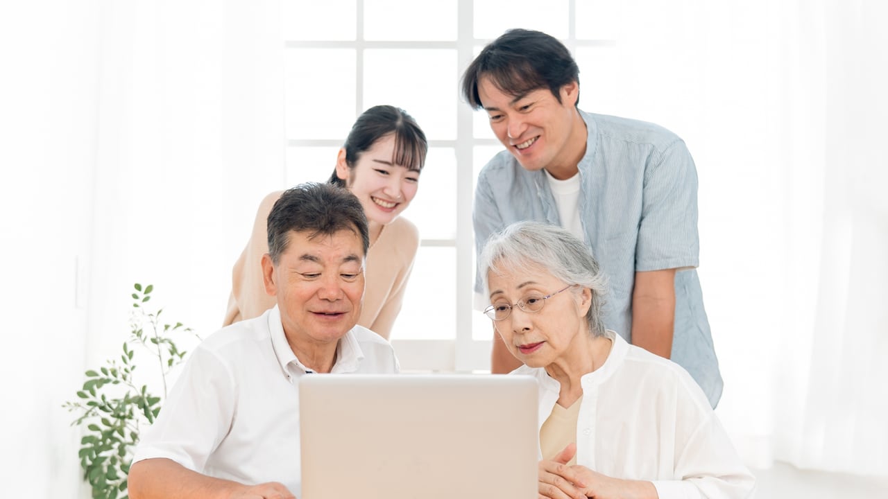 高齢の両親と一緒に、パソコンで調べものをする家族のイメージ
