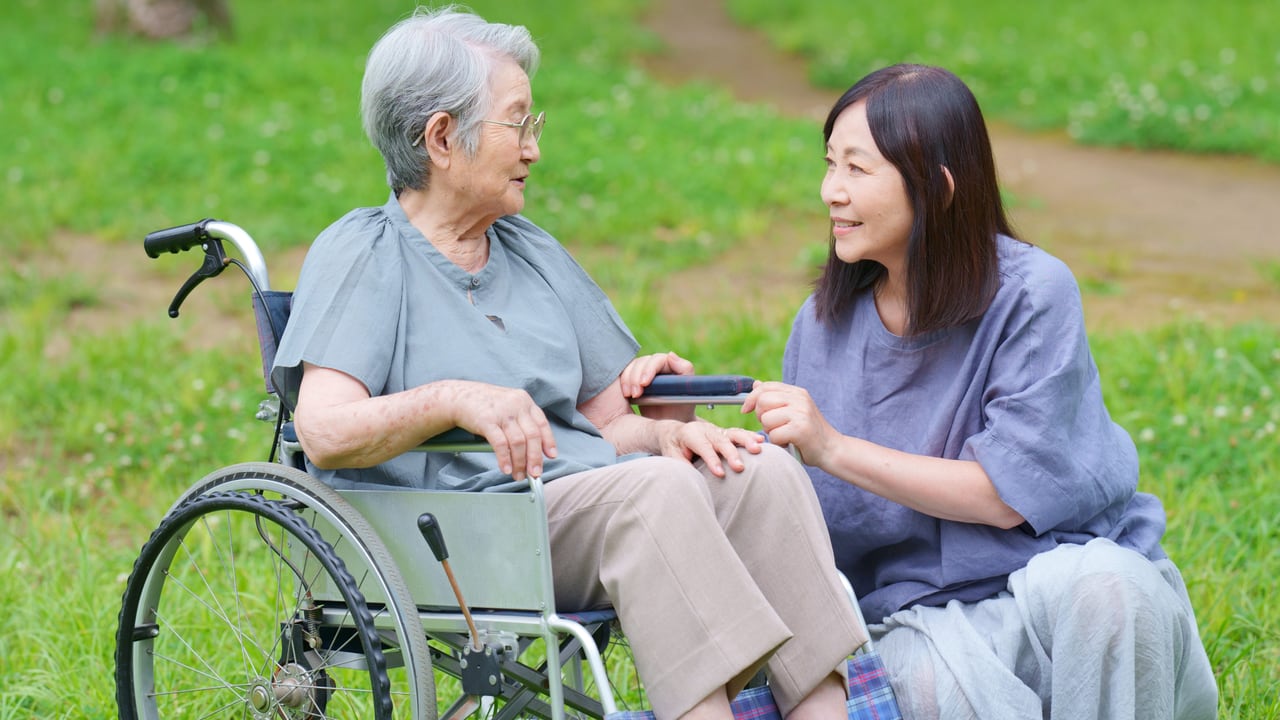 車椅子の母に寄り添い、話をする娘のイメージ