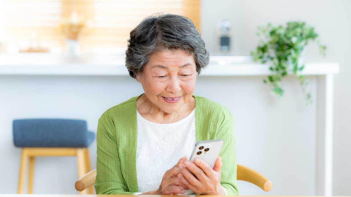 スマートフォンを手に微笑む高齢の女性のイメージ