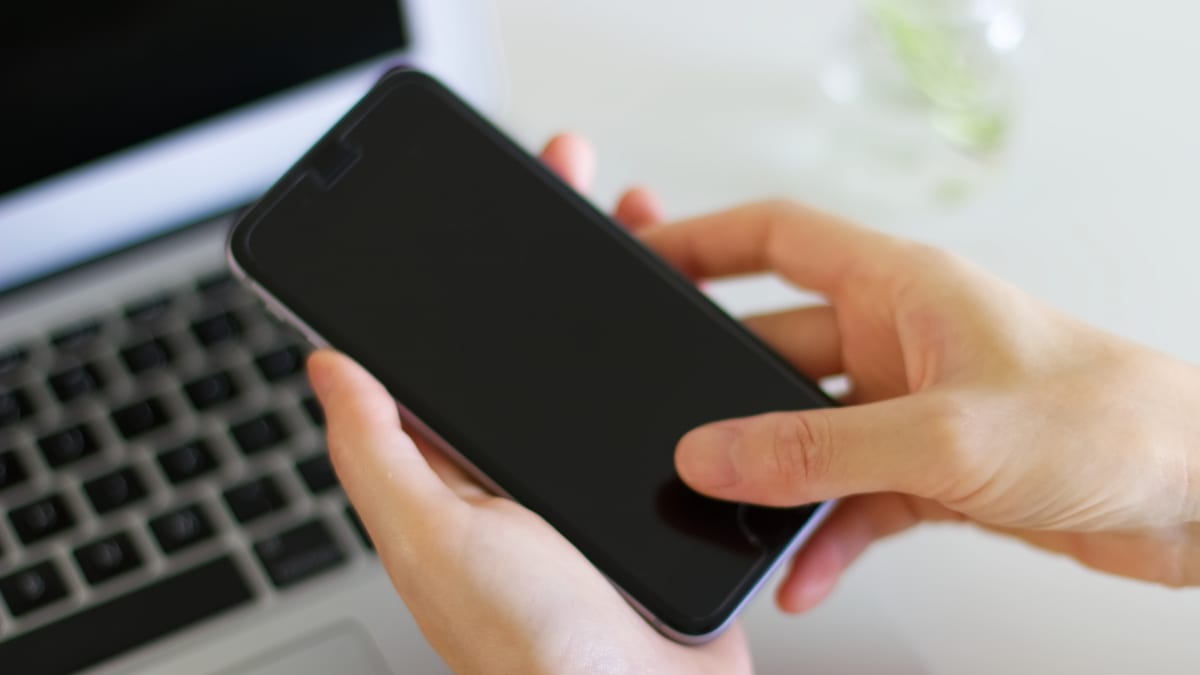 パソコンの前でスマートフォンを操作する手元のイメージ